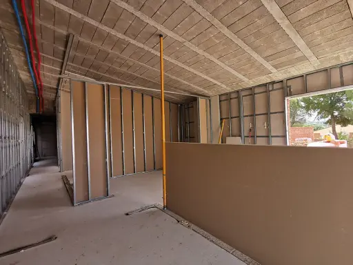 Construcción interior con estructura metálica y paneles de **ladrillo o pladur**. Se ven tuberías de agua y un nivelador.