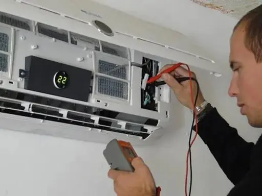 Técnico revisa unidad interior de aire acondicionado con multímetro, cumpliendo la normativa de instalación.