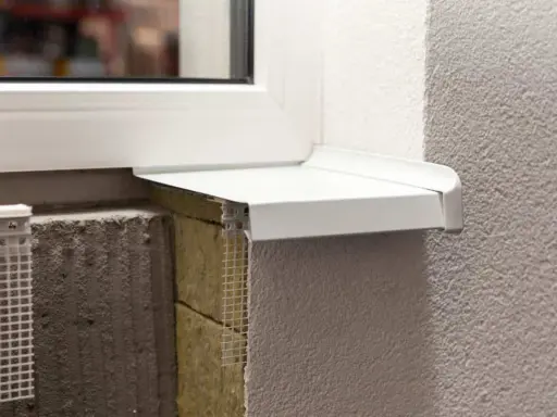 Detalle constructivo de un alféizar blanco sobre aislamiento y mampostería, con malla de refuerzo visible.