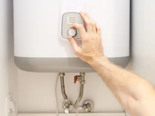 Mano ajustando el termostato de un termo eléctrico. Posiblemente para solucionar problemas de agua caliente.