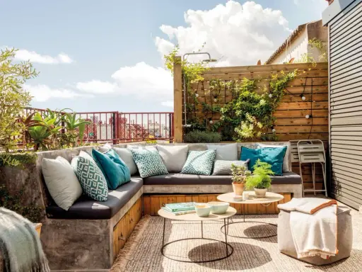 Un rincón perfecto para hacer una terraza: sofá de obra con cojines turquesas, mesas bajas y plantas.