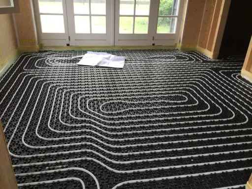 Instalar suelo radiante: tuberías blancas sobre paneles negros, listas para cubrir. Planos en el suelo.