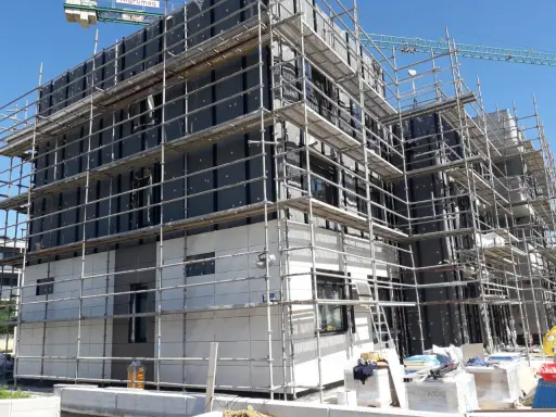 Edificio en construcción con andamios cubriendo la fachada. Se aprecian materiales de aislamiento y paneles, cumpliendo la ley de fachadas.