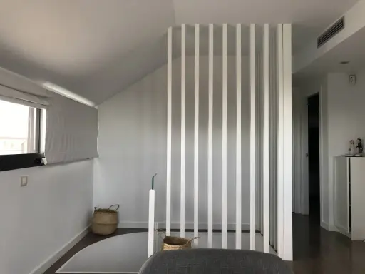 Modern interior with a white slatted divider, suggesting a design to tirar tabique para unir dos habitaciones. Baskets and a window add warmth.