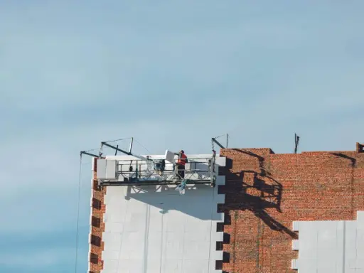 Trabajadores en una plataforma suspendida instalan paneles aislantes en un edificio, parte de un proyecto de sate.