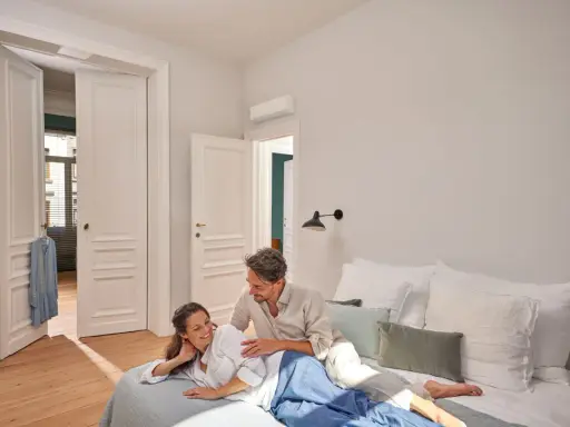Pareja relajándose en la cama, con el aire acondicionado en modo noche creando un ambiente perfecto.