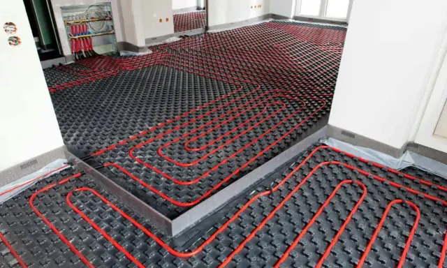 Instalación de un sistema de calefacción por suelo radiante enfria. Tubos rojos serpentean sobre paneles negros en una habitación en construcción.