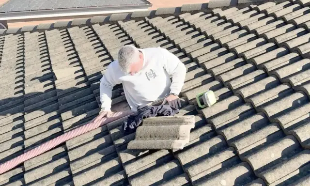 Hombre en tejado trabajando en el aislamiento térmico del tejado. Se ve una manguera rosa y una herramienta verde.