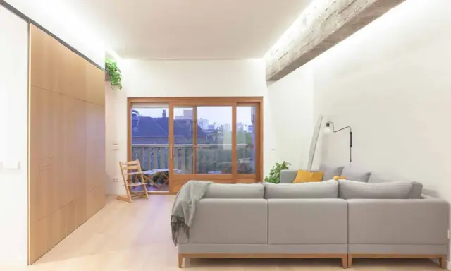 Salón moderno con sofá gris, grandes ventanales y **techos con vigas de hormigón decorar** el espacio con estilo industrial.