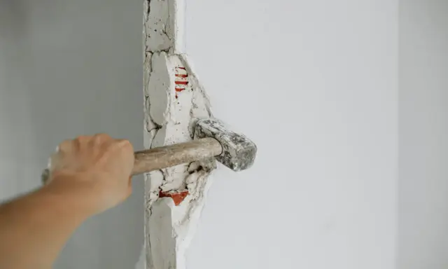 Mano golpeando un tabique con un martillo. La pregunta de cuanto se tarda en tirar un tabique depende de la habilidad y el material.