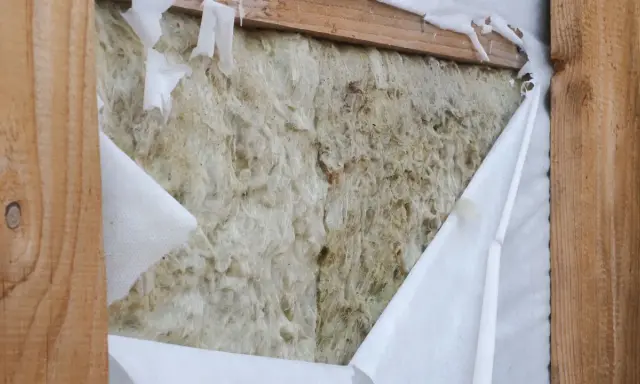 Aislamiento de lana de roca expuesto, con una barrera de vapor blanca rasgada que revela la textura fibrosa.