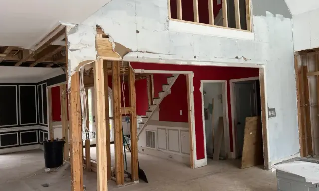Interior en proceso de demolición, mostrando la estructura de madera expuesta y el cableado. Se observa una escalera roja y paredes parcialmente derribadas, como si se estuviera planeando como tirar una pared de casa.