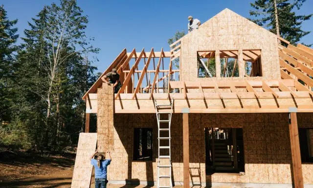 Obreros trabajan en la estructura de madera de una casa, mostrando los pasos a seguir para construir una casa.