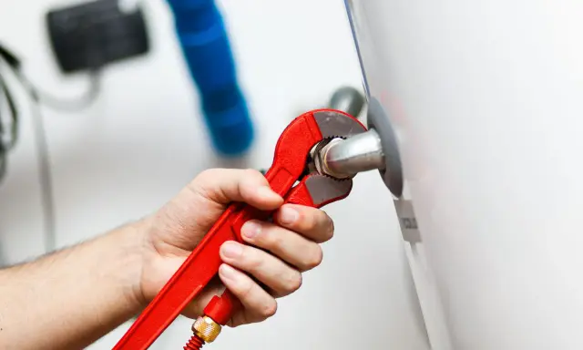 Mano con llave roja ajustando tubería. Es parte de la revisión caldera gas obligatoria para garantizar seguridad y eficiencia.