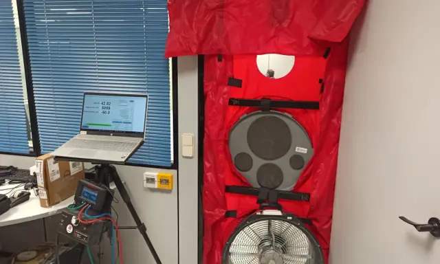 Equipo para blower door test en puerta, con laptop mostrando datos y medidor de presión.