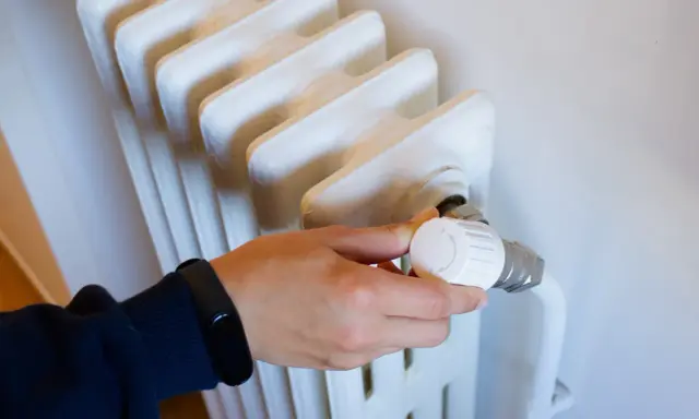 Mano ajustando el termostato de un radiador, parte de los contadores individuales de calefacción central.