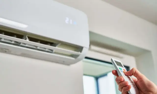 Mano ajustando el control remoto de un aire acondicionado para que gasta menos. La pantalla muestra 21 grados.