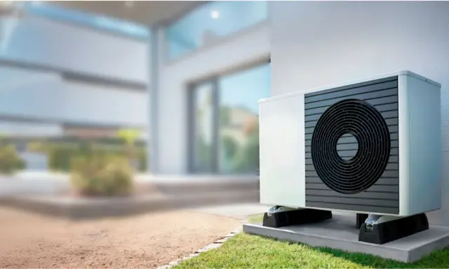 Unidad exterior de bomba de calor instalada junto a una casa moderna, lista para climatizar el piso.