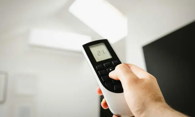 Mano ajustando el mando de aire acondicionado a 21 grados. Instrucciones claras para un confort óptimo.