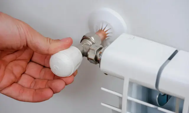 Mano ajustando la perilla de un radiador, mostrando partes de un radiador de agua como la válvula y la conexión.