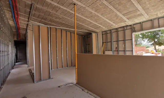 Construcción interior con estructura metálica y paneles de **ladrillo o pladur**. Se ven tuberías de agua y un nivelador.