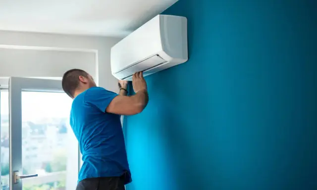 Hombre instalando aire acondicionado uno mismo en pared azul.