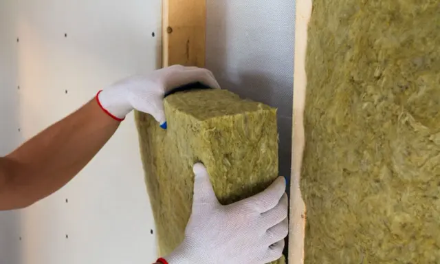Manos enguantadas colocan aislamiento de lana de roca para saber como aislar termicamente una habitacion.