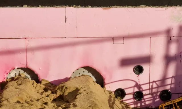 Aislamiento rosa para cimentación, con arena y tuberías. Su baja transmitancia térmica es clave para la eficiencia energética.