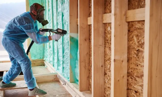 Un trabajador con equipo de protección rocía espuma aislante, mostrando la diferencia entre poliuretano y poliestireno en la construcción.