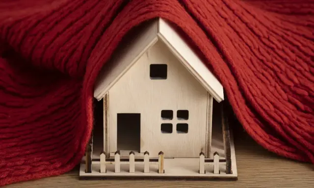 Casa de madera envuelta en manta roja, simbolizando la normativa de aislamiento térmico en viviendas para mantener el calor.