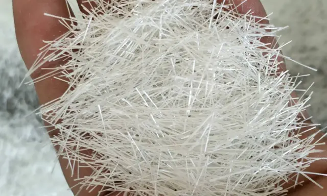 Mano sosteniendo un puñado de fibra de vidrio aislante, que puede ser tóxico.