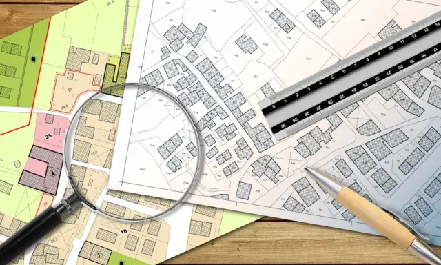 Planos de parcelas con lupa, regla y bolígrafo. Se analiza la diferencia entre edificabilidad y ocupación en urbanismo.