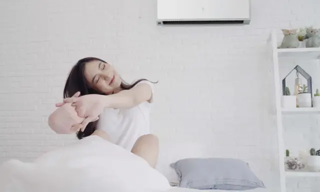 Mujer estirándose en la cama bajo el aire acondicionado, ideal para saber como poner el aire acondicionado para dormir y disfrutar de un descanso fresco.