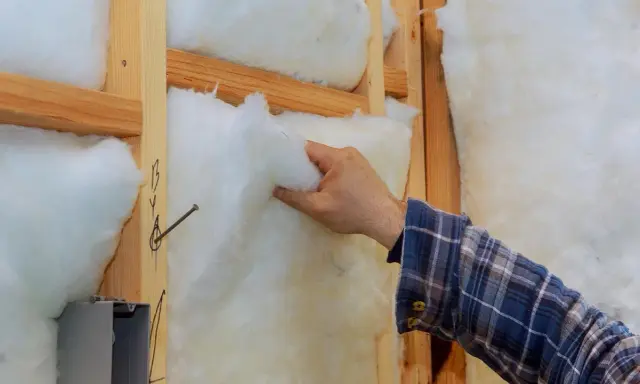 Mano colocando aislamiento en la pared de madera. Mejora el aislamiento de edificios para mayor eficiencia energética.