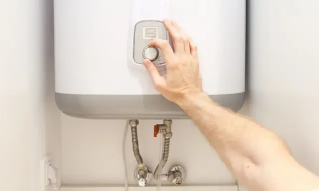 Mano ajustando el termostato de un termo eléctrico. Posiblemente para solucionar problemas de agua caliente.