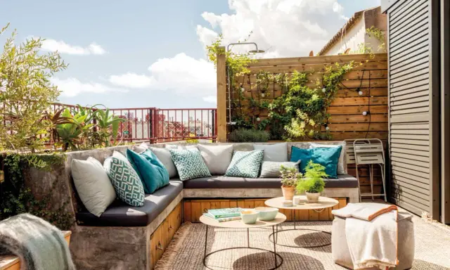 Un rincón perfecto para hacer una terraza: sofá de obra con cojines turquesas, mesas bajas y plantas.