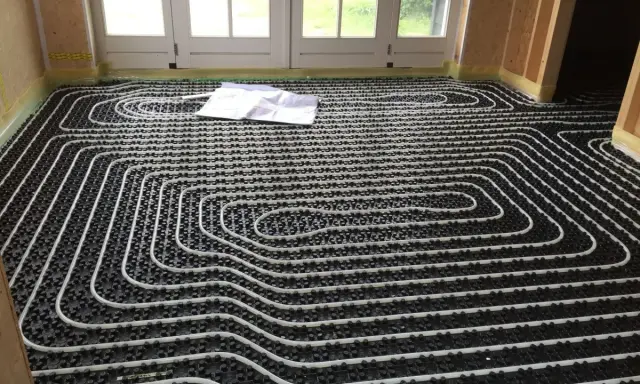 Instalar suelo radiante: tuberías blancas sobre paneles negros, listas para cubrir. Planos en el suelo.