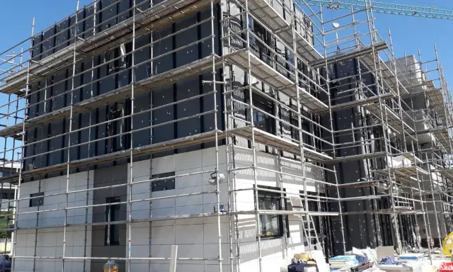 Edificio en construcción con andamios cubriendo la fachada. Se aprecian materiales de aislamiento y paneles, cumpliendo la ley de fachadas.