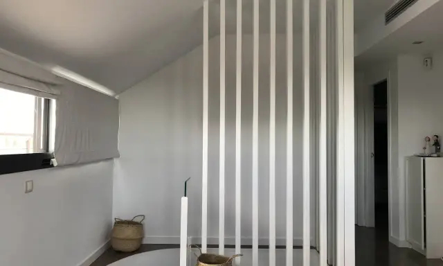 Modern interior with a white slatted divider, suggesting a design to tirar tabique para unir dos habitaciones. Baskets and a window add warmth.