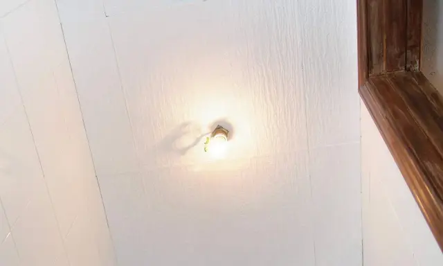 Techo con paneles de poliestireno extruido, una bombilla encendida y un marco de madera.