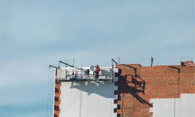 Trabajadores en una plataforma suspendida instalan paneles aislantes en un edificio, parte de un proyecto de sate.