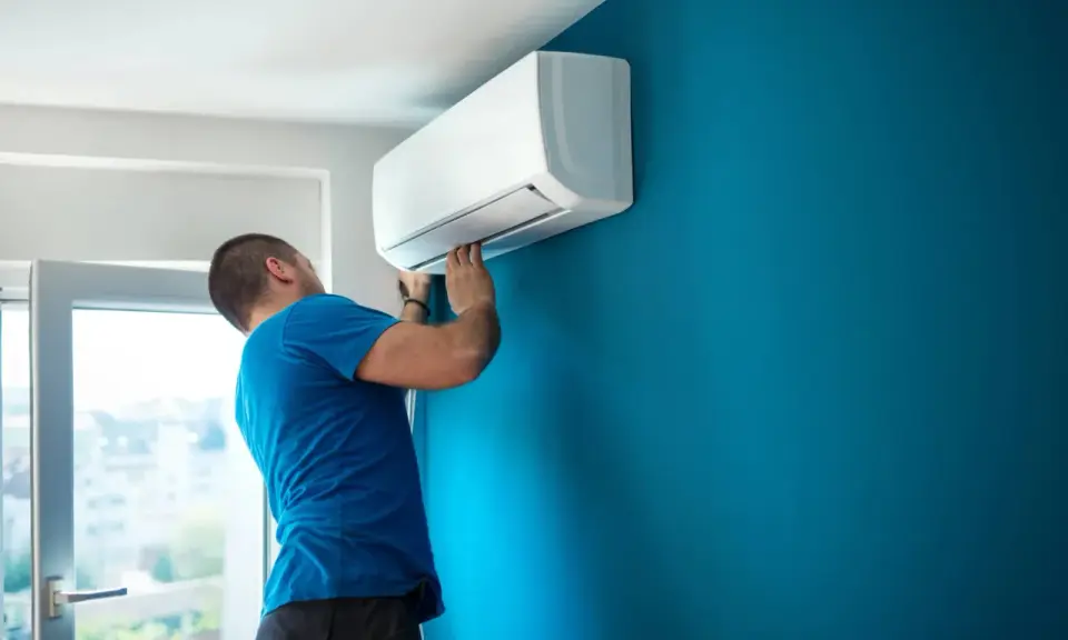 Hombre instalando aire acondicionado uno mismo en pared azul.