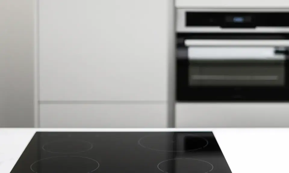 Placa vitrocerámica negra lista para instalar junto a un horno empotrado en una cocina moderna.