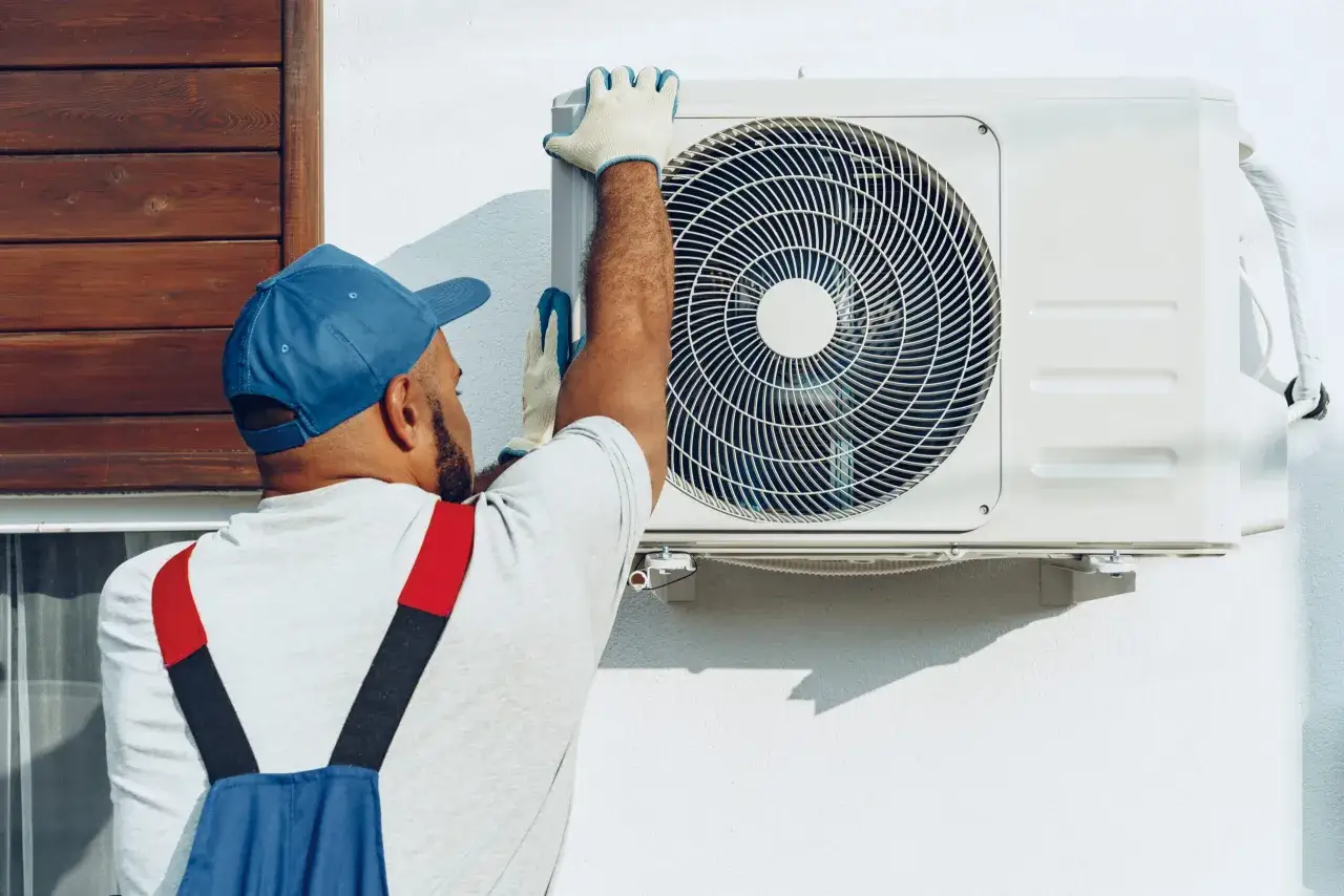 Técnico con guantes realiza mantenimiento a bomba de calor exterior.