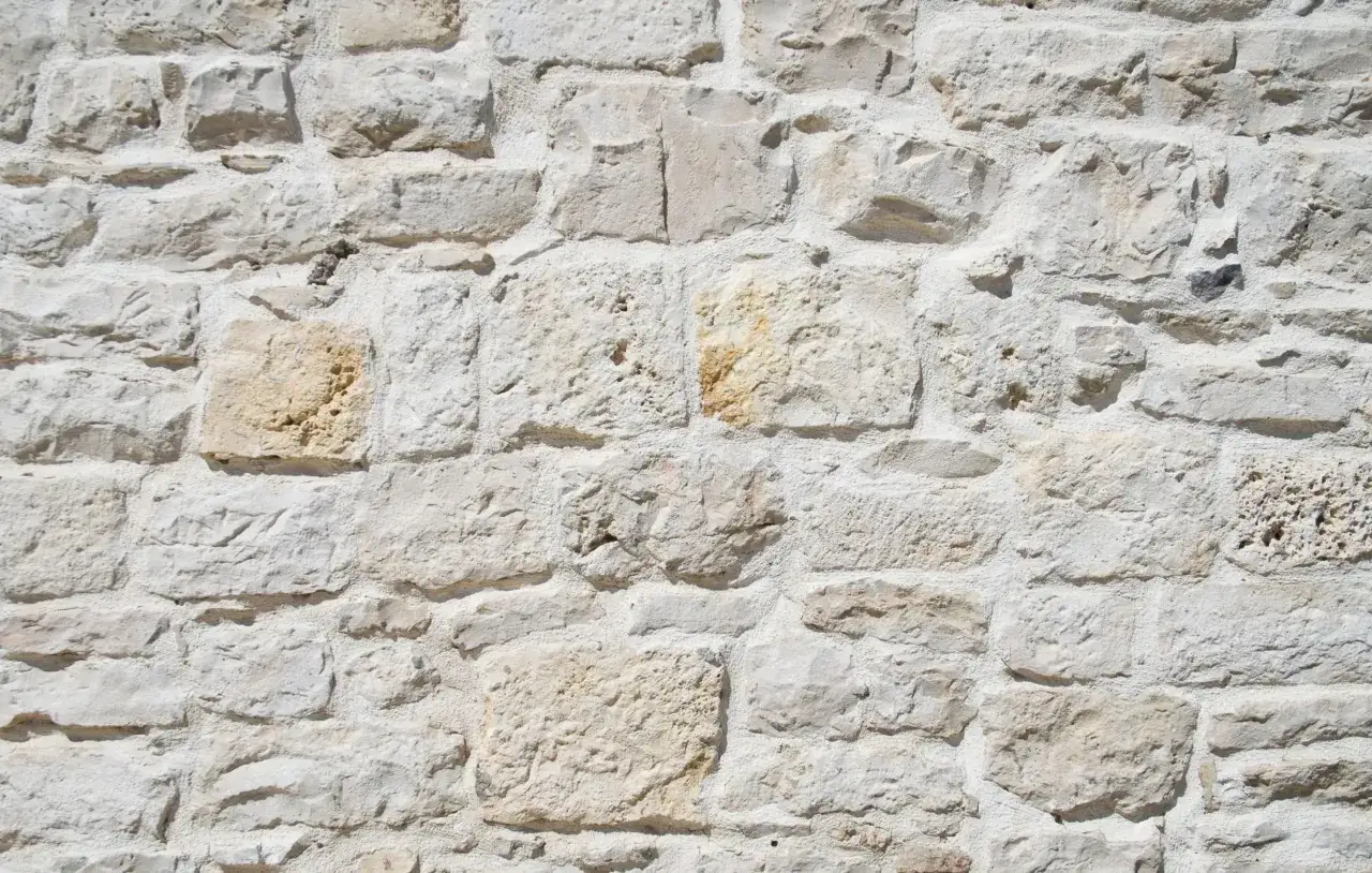 Muro de piedra con mortero de cal, mostrando la textura r&uacute;stica y el color claro de las piedras unidas.
