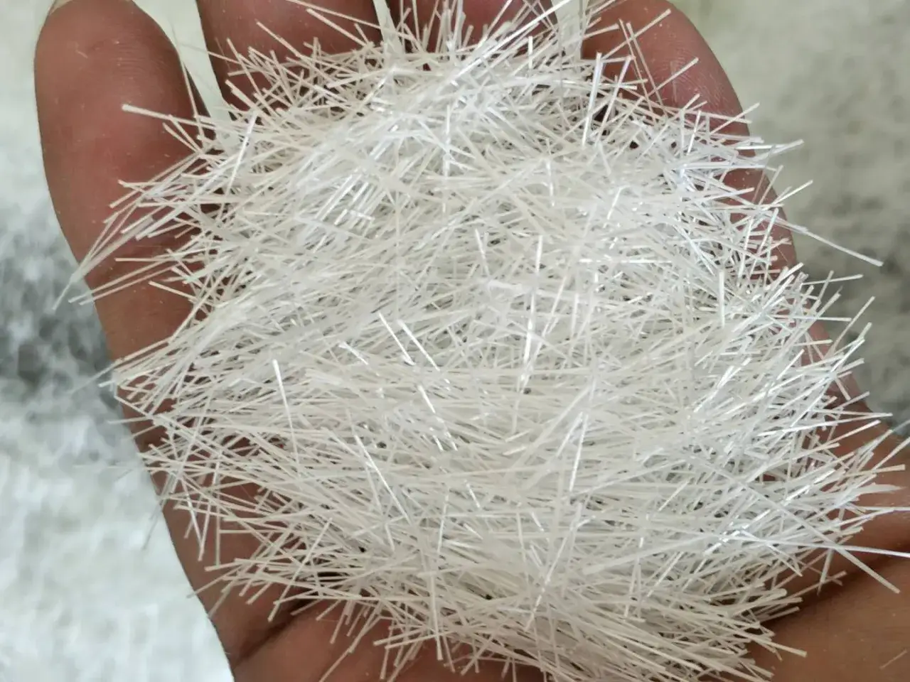 Mano sosteniendo un puñado de fibra de vidrio aislante, que puede ser tóxico.