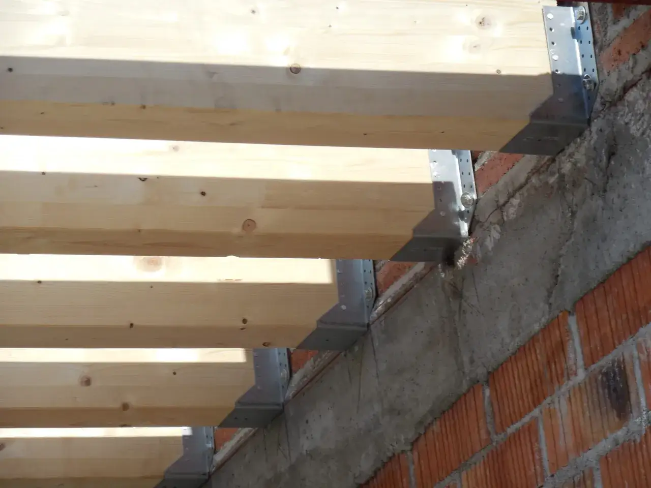 Detalle de la construcci&oacute;n: se ven vigas de madera reci&eacute;n colocadas, sujetas con soportes met&aacute;licos a una pared de ladrillo y hormig&oacute;n.