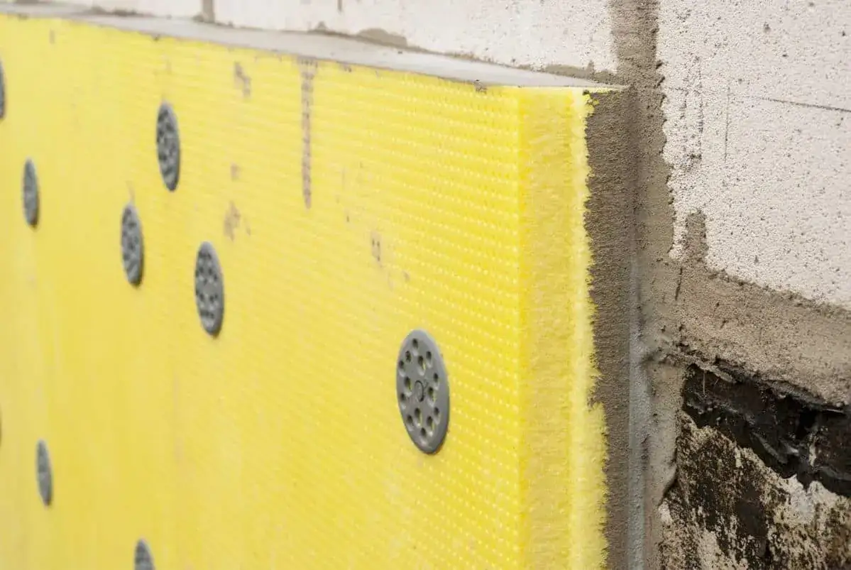 Placa de poliestireno amarillo con fijaciones circulares grises, parte de un sistema de aislamiento exterior.