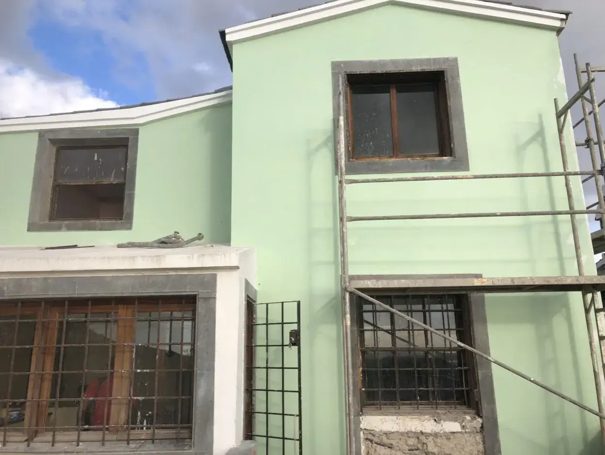 Fachada de casa en construcción, color verde pálido. Andamios y ventanas con rejas. ¿Cuántos metros cuadrados se pueden construir sin proyecto?