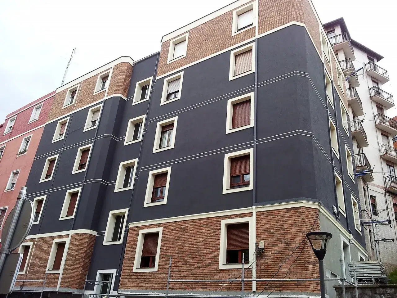 Edificio moderno con fachada de ladrillo y estuco gris, cumpliendo la ley de fachadas. Ventanas rectangulares con persianas marrones.